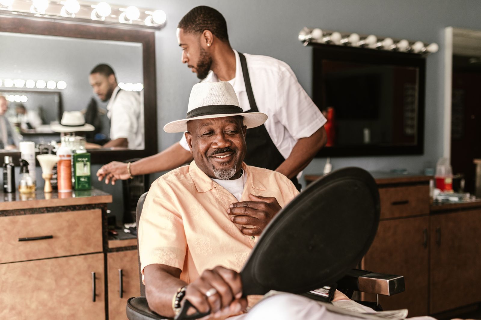 Cliente sonriente con sombrero en el sillón de una barbería mientras el barbero le atiende
